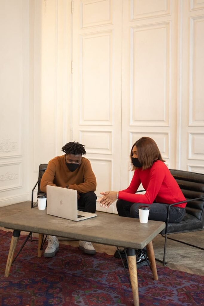 Multiracial colleagues in masks sitting at table with laptop in light room